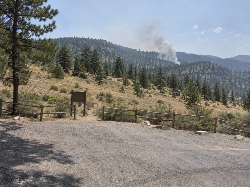 Camera still: a thin column of gray smoke rising from a dry hillside above a trailhead
